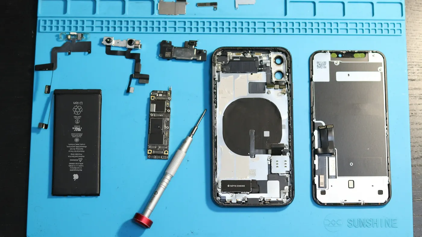 Smartphone parts and a screwdriver laid out on a blue repair mat